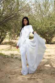 Woman in a white outfit standing in a natural setting with trees and dirt ground.